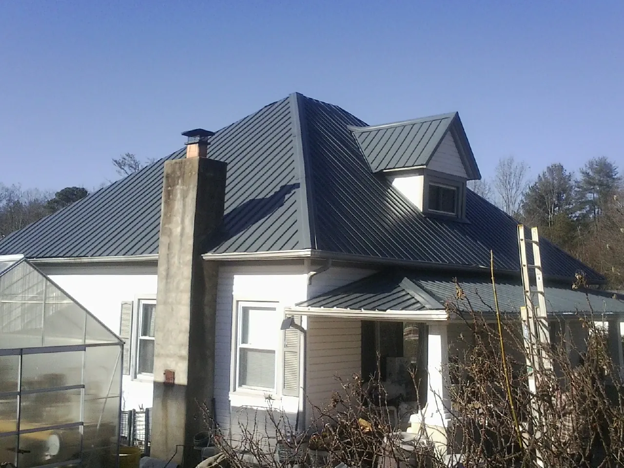 Dark blue standing seam metal roof on a white farmhouse with dormer — Slate & Tile Roof Repair by Roofing Brothers in Mexia