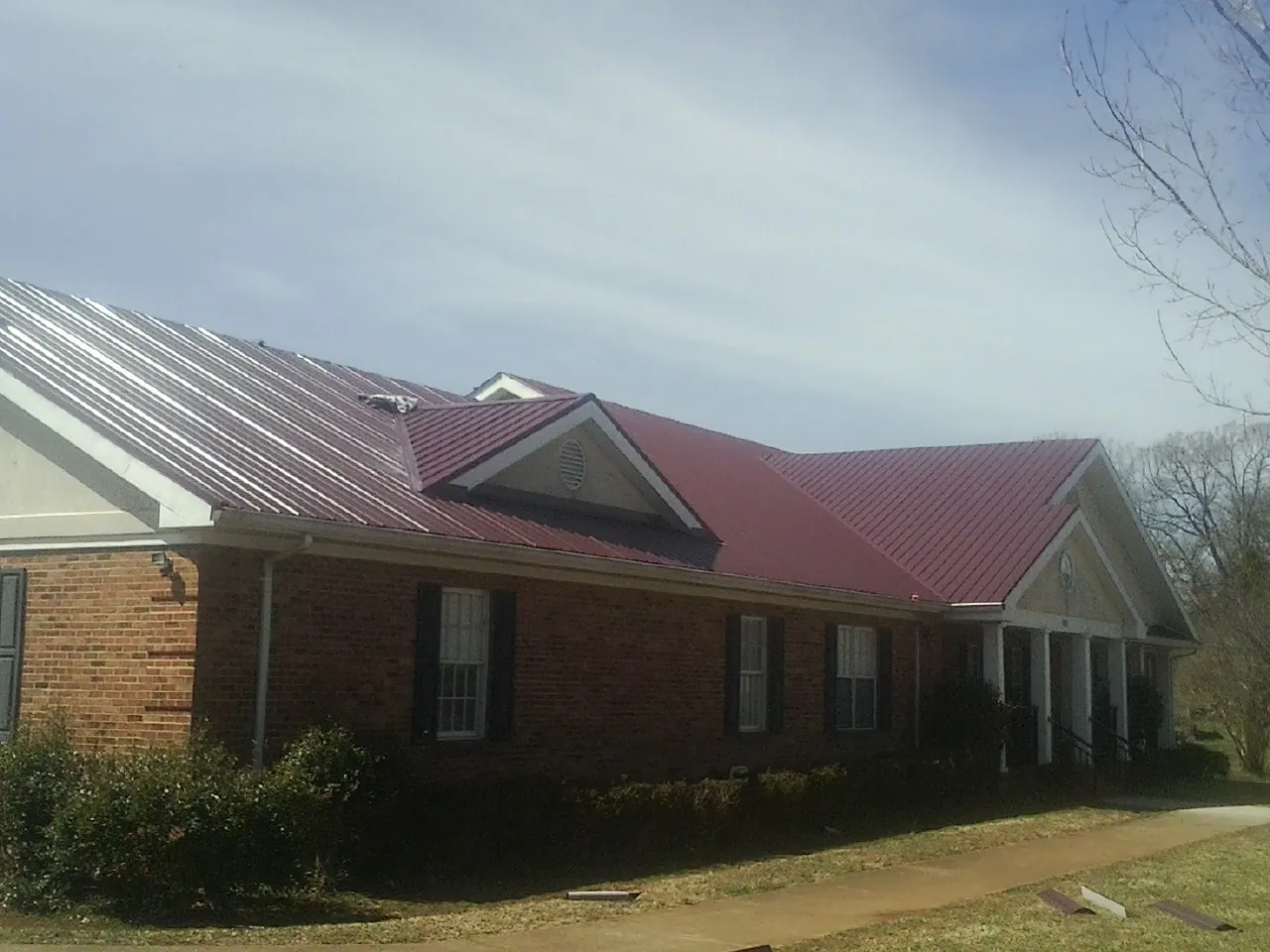 Red metal roof with gabled entries on a long brick building, from a Hail Damage Roof Repair job in Mexia