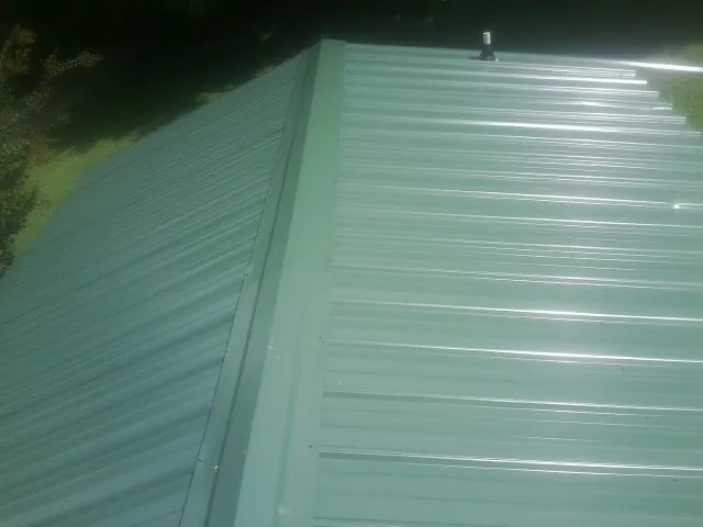 New green metal panels meeting at the ridge of a roof — Flat Roof Repair work by our crew in Mexia