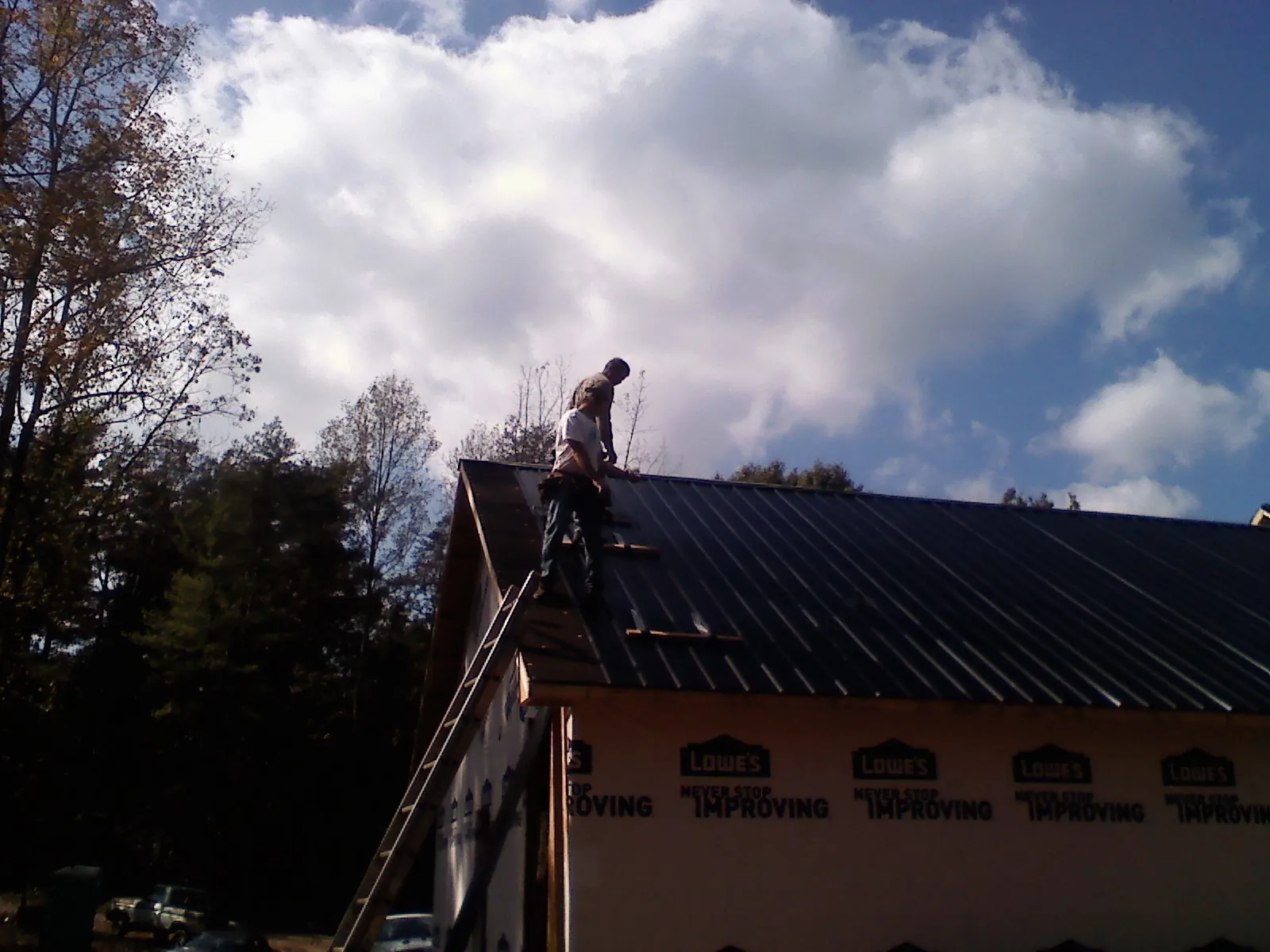 Roofer fastening dark metal panels high against a cloudy sky, from a Roof Inspection job in Mexia