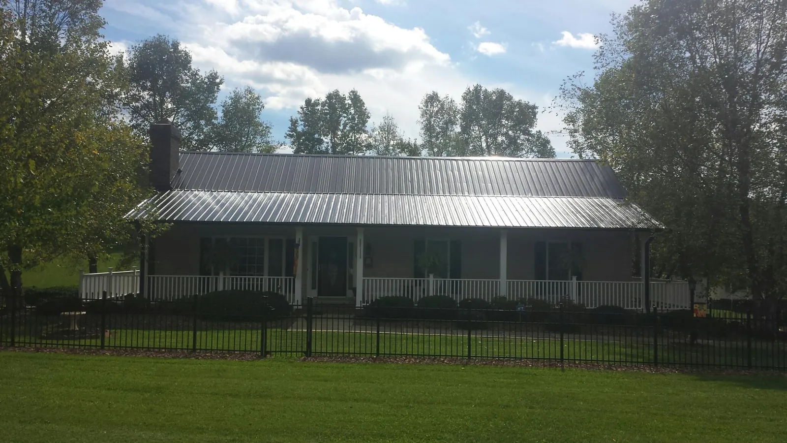 Gray metal roof on a brick ranch with a full width front porch — Gutter Guard Installation work by our crew in Mexia