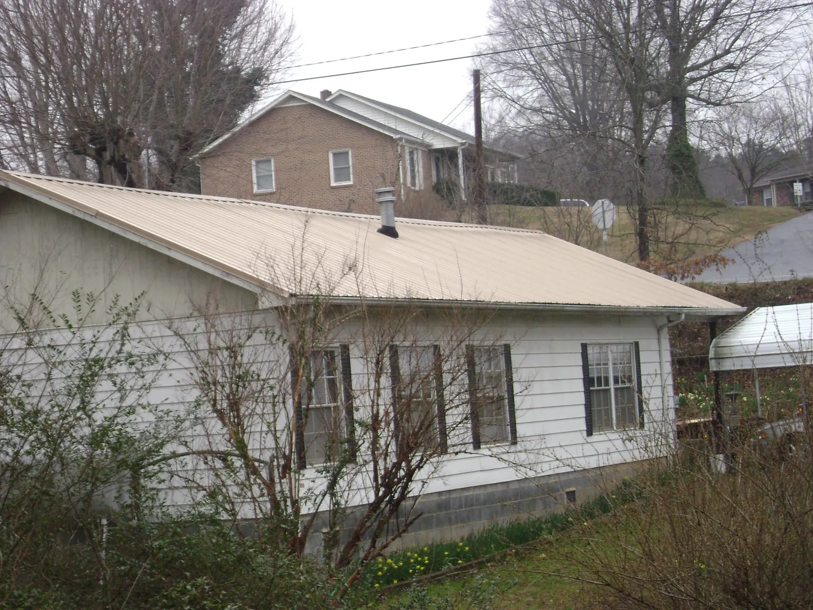 Tan metal roof on a white sided house set into a hillside — Commercial Roofing by Roofing Brothers in Mexia