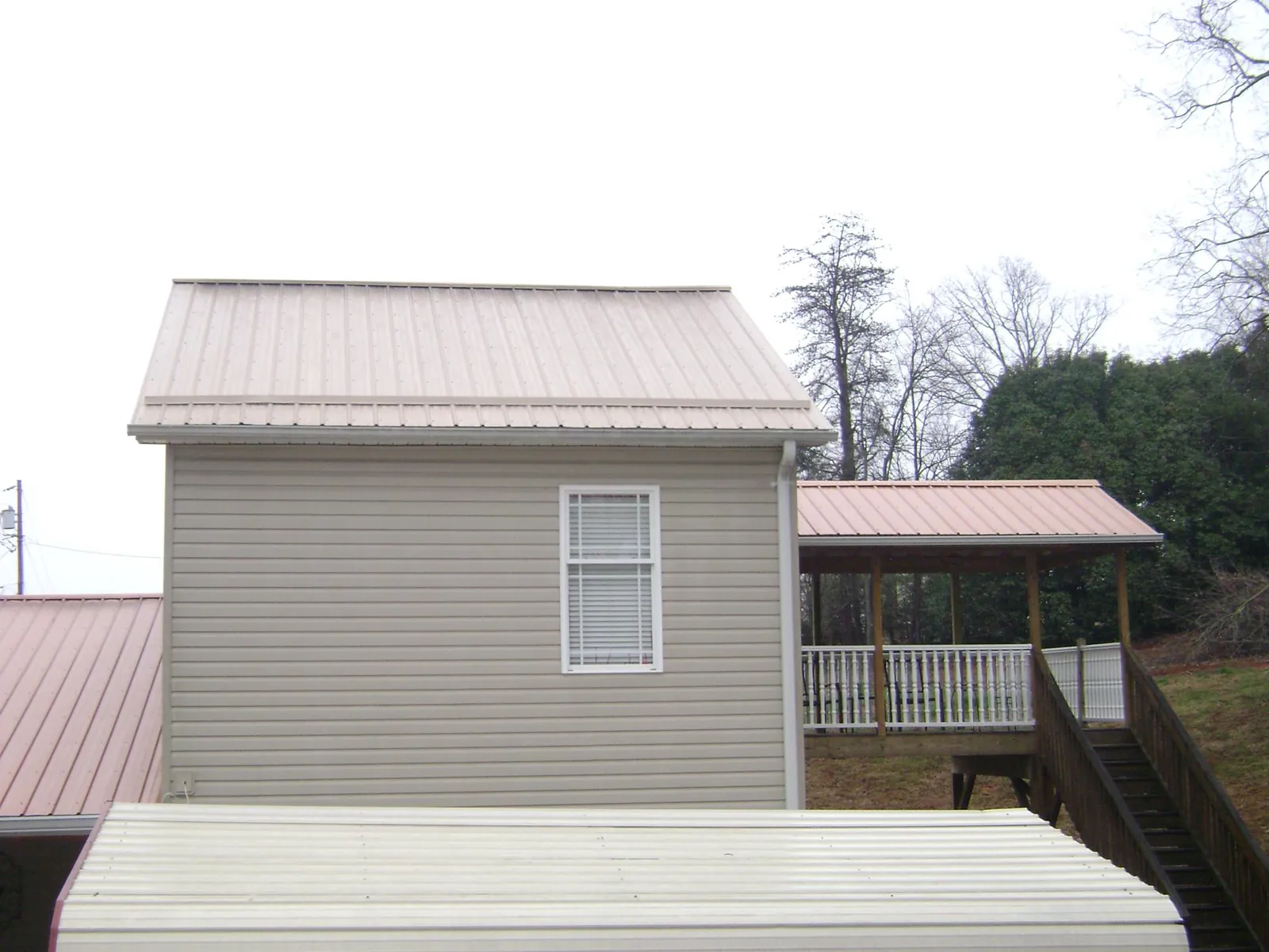 Tan metal roofs on a two story addition and attached porch, from a Roof Replacement job in Mexia